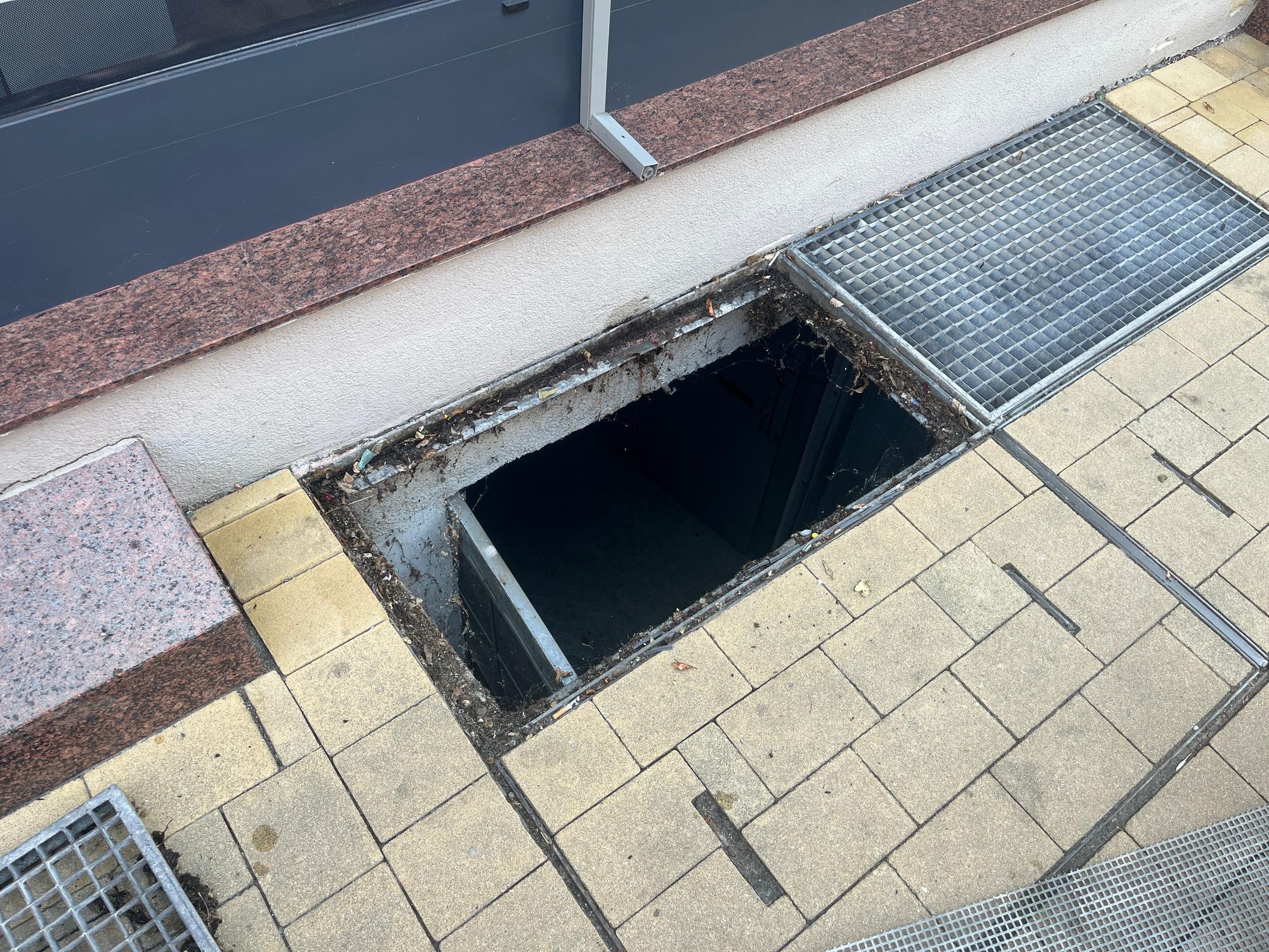 Offener Schacht mit Metallgitter und Granitverkleidung auf Gehweg