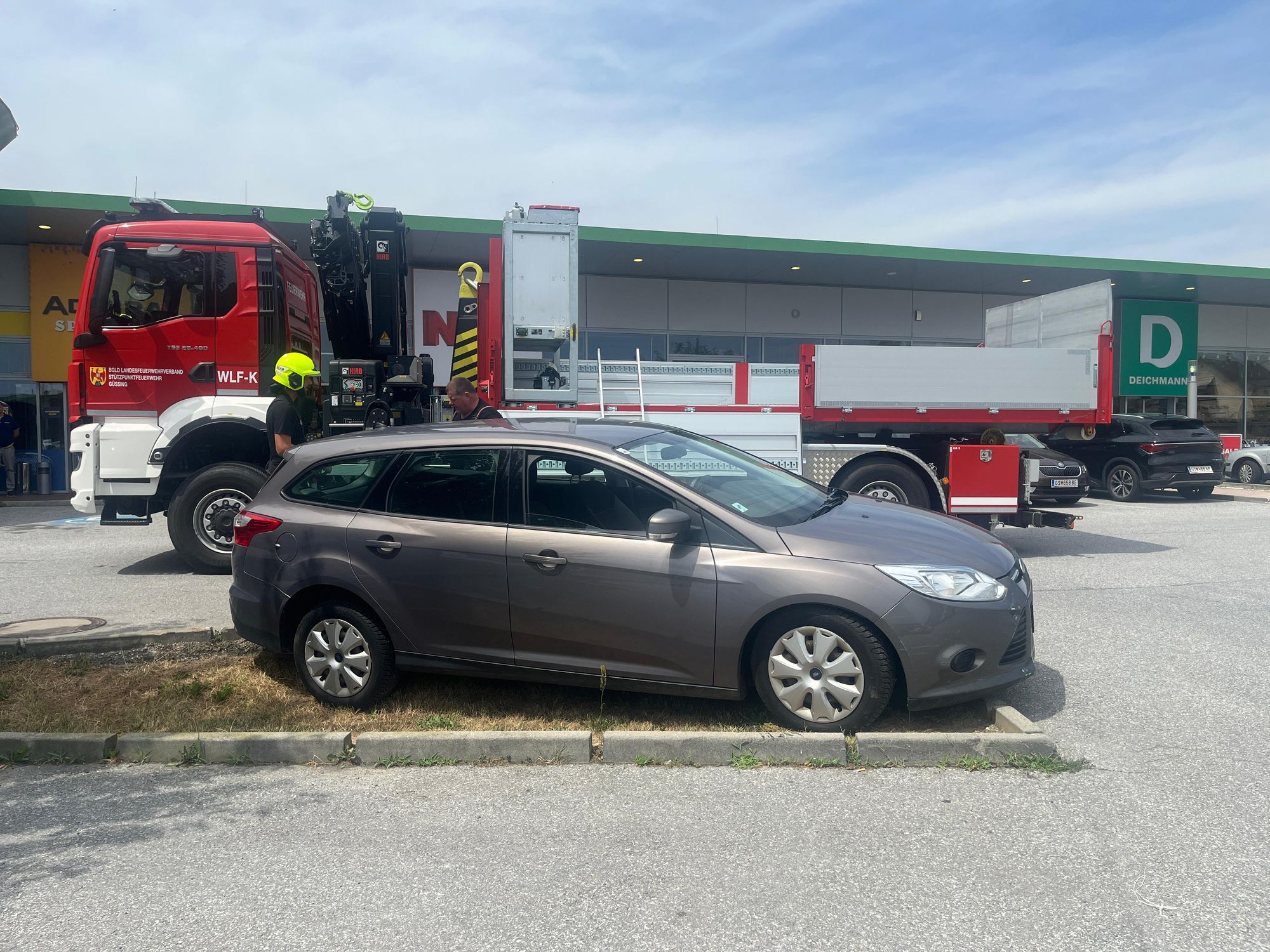 Feuerwehrfahrzeug mit Kran und zwei Männern neben einem grauen Kombi in Gossing